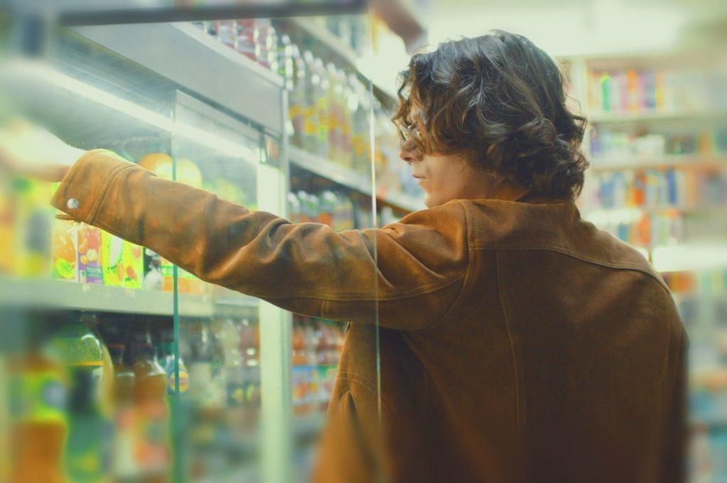 comment choisir son huile de CBD : un jeune homme au cheveux long se sert dans un rayon frais d'une épicerie. 