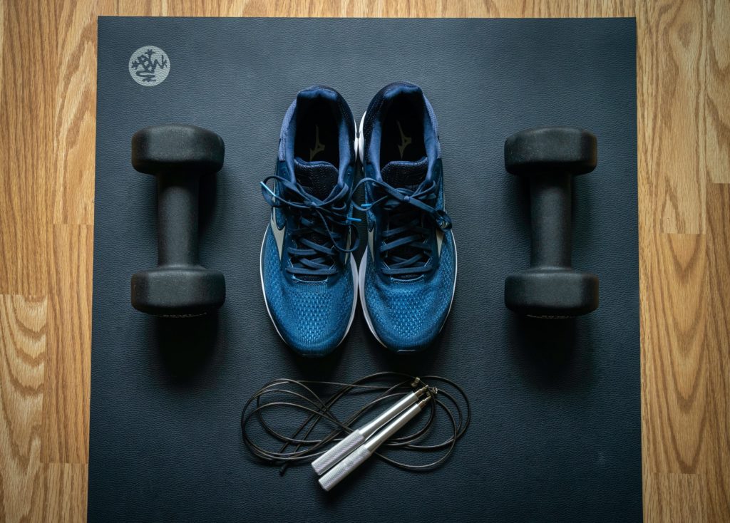 Des baskets bleus sont posés sur un tapis de sport avec des poids et une corde à sauter.